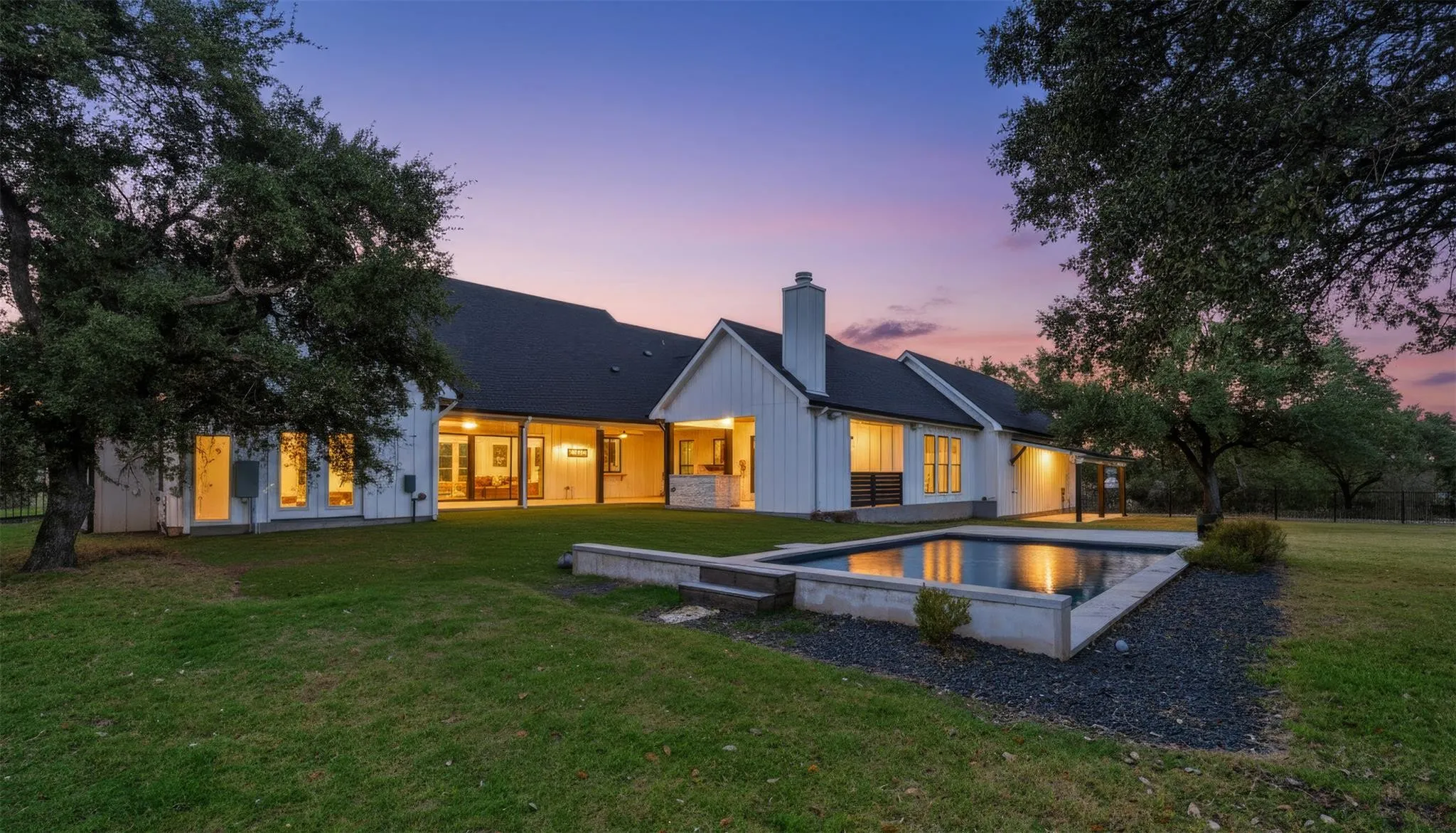 White farmhouse at dusk with warm lights and a reflecting pool