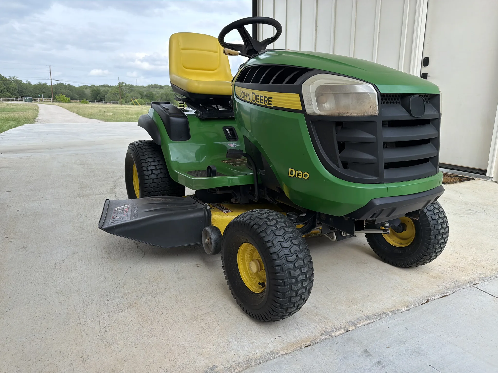 Green riding mower parked beside a metal barn